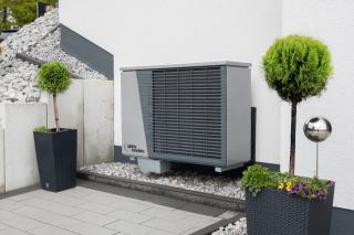 Unite exterieure de pompe a chaleur posee sur un socle le long d'un mur de maison